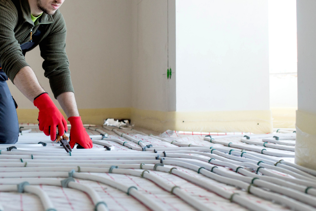 Tecnico con guanti rossi installa tubature per il riscaldamento a pavimento in una stanza.